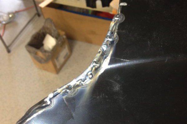 To add metal to the edge of a panel, first find a wire that is a little bigger than the area that’s being filled, bend it to fit the shape, and carefully tack it to the edge. Then weld it on, one little stitch at a time. Allow the metal to cool before welding each stitch, so you don’t burn away the little wire.