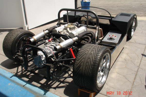 The “roller skate” is nearly complete, with drivetrain installed, ready for the rear body clip. The custom fabricated suspension is visible in the foreground. The red support placeholders were later replaced with Alden coilover shocks.